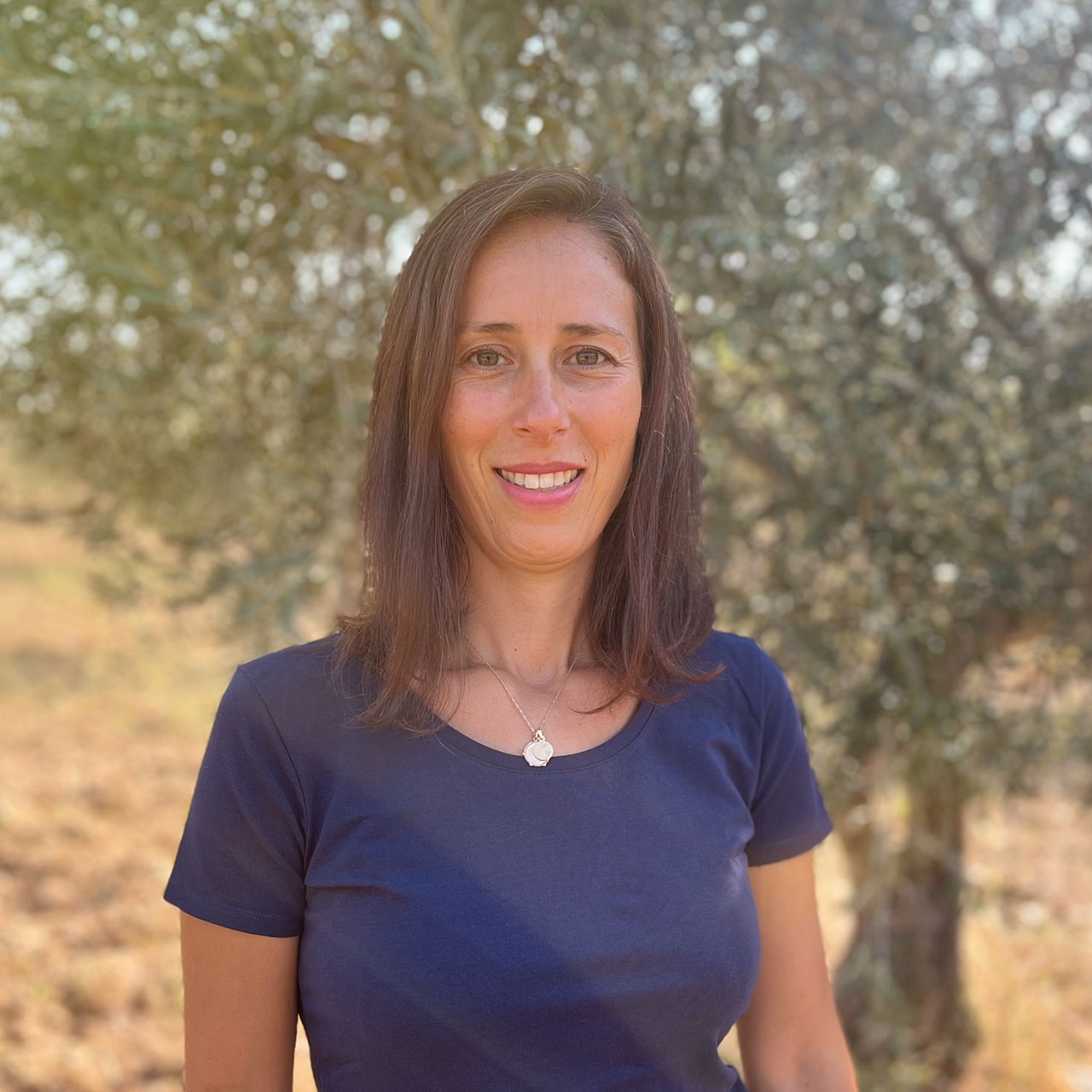 Ein Portraitfoto von Lidia, aufgenommen vor einem Olivenbaum im Sonnenschein.