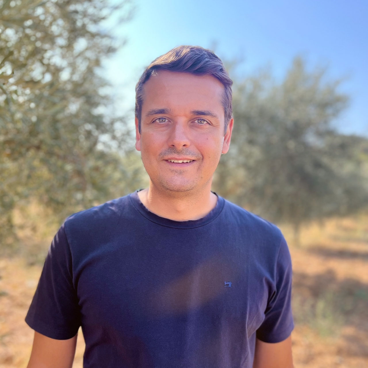 Ein Portraitfoto von Laki, aufgenommen vor einem Olivenbaum im Sonnenschein.